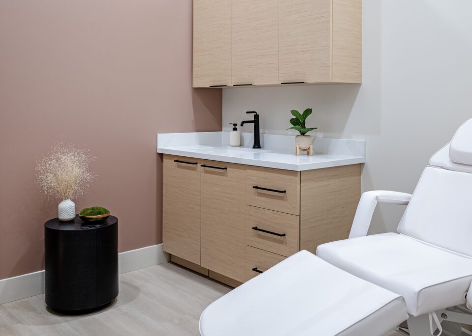 Elase Sarasota treatment room featuring white adjustable chair, dusty rose accent wall, and light wood medical cabinetry