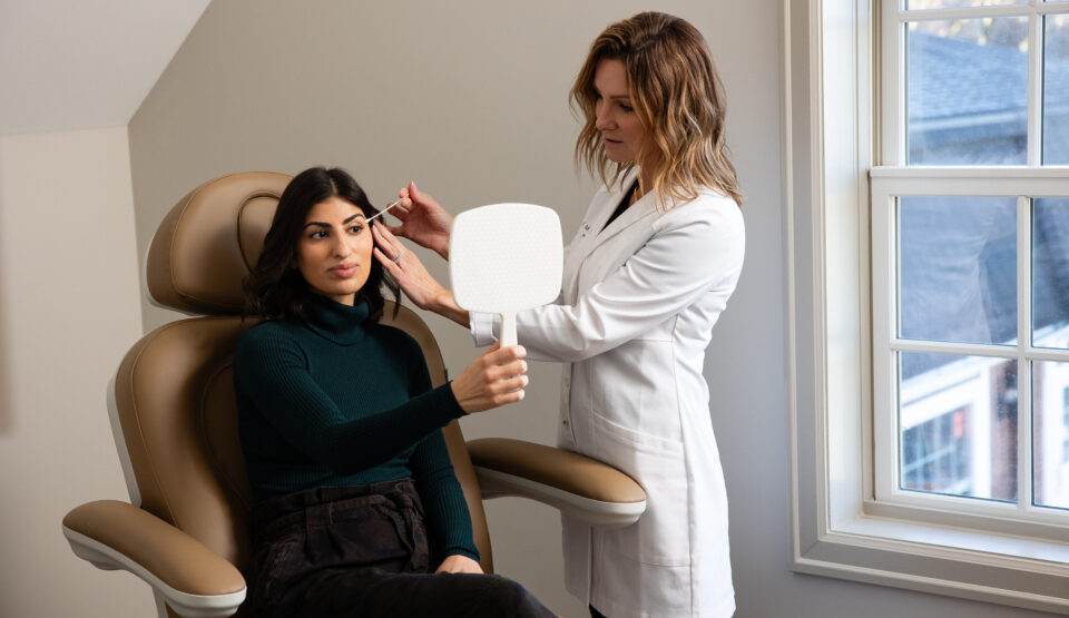 A licensed aesthetic provider at Elase Med Spa prepares to administer a Botox treatment while a client reviews her appearance in a handheld mirror during consultation near Chicago.