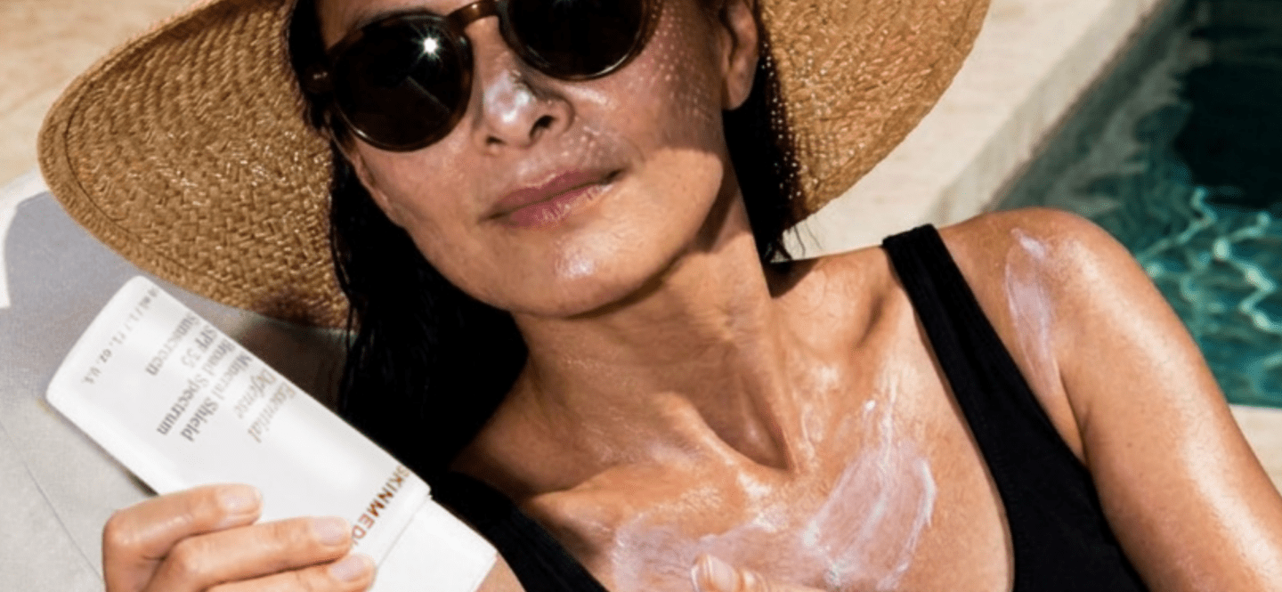 A woman in a black swim suit and sunhat applying Skinmedica sunscreen